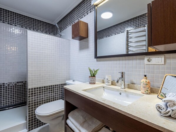 A bathroom with a white toilet, a sink with a mirror above it, and a towel rack. - Luxury Suite Tendillas (Granada)