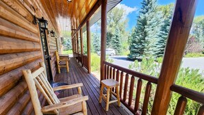 Eine hölzerne Veranda mit Schaukelstühlen und einem kleinen Tisch, mit Blick auf eine bewaldete Gegend.