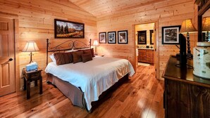 Ein Schlafzimmer einer Holzhütte mit Bett, Nachttischen, Deckenventilator, gerahmten Bildern und einem Aquarium.