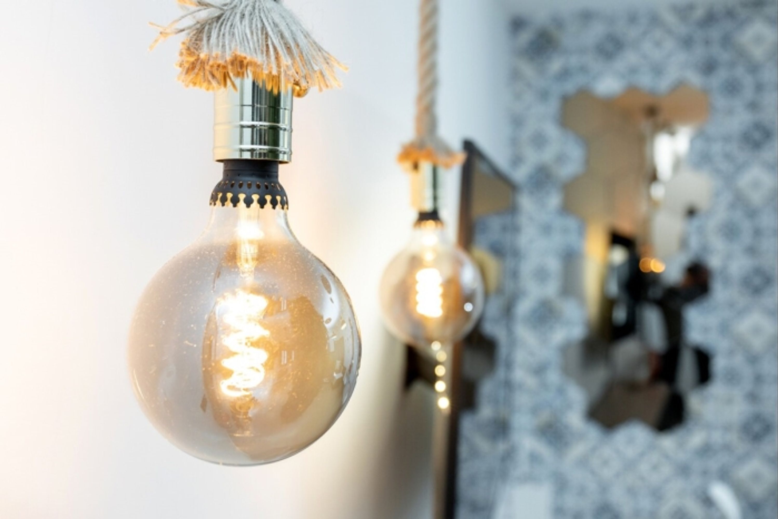 Gros plan d’une ampoule suspendue, dont on peut voir le filament et qui est ornée d’une frange décorative.