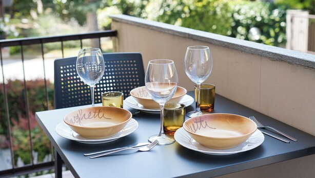 Une table dressée avec des assiettes, des verres et des couverts sur un balcon donnant sur un paysage verdoyant.