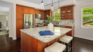 A modern kitchen with wooden cabinets, a stainless steel refrigerator, a microwave, and a large island with bar stools. - Pili Mai at Poipu 15b By Parrish Kauai - spacious condo great for families! (Koloa)