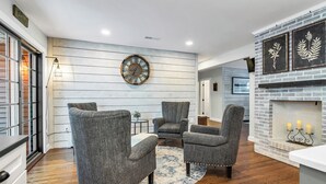 A modern living room with a fireplace, grey upholstered chairs, a round wall clock, and a rustic wooden wall. - Andover in-town, upscale furnished home, single level living & 2-car garage (Andover)