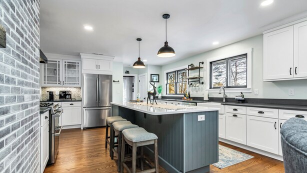 A modern kitchen with a central island, bar stools, a refrigerator, and a brick accent wall. - Andover in-town, upscale furnished home, single level living & 2-car garage (Andover)