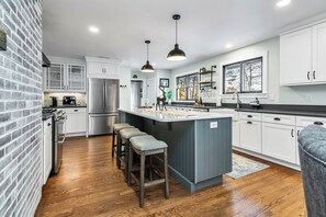 A modern kitchen with a central island, bar stools, a refrigerator, and a brick accent wall.