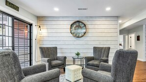 A modern living room with grey upholstered armchairs, a white ottoman, and a round wall clock. - Andover in-town, upscale furnished home, single level living & 2-car garage (Andover)