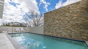 A swimming pool with a stone wall, lounge chairs, and a clear sky. - Spacious 2 bedroom Apartment Near PA Hospital (Woolloongabba)