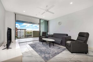 Una sala de estar moderna con sofá, sillón y mesa de centro, ventilador de techo y vista a través de un vidrio.