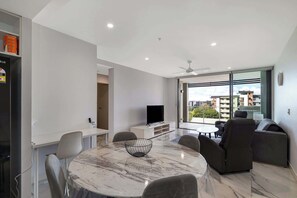 Un soggiorno moderno con un tavolo in marmo, posti a sedere confortevoli, una televisione a schermo piatto e un balcone con vista sulla città.