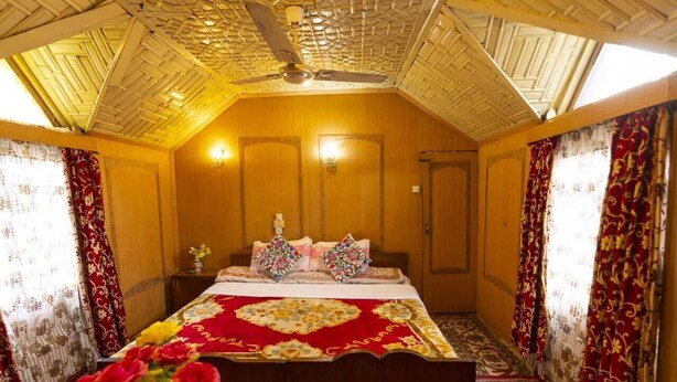 A traditional room with a wooden ceiling, a bed with a red and gold bedspread, and curtains with a floral pattern. - N Mumbai Group Of House Boat (Srinagar)