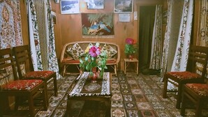 A room with a patterned floor, a sofa, two wooden chairs, a small table with a vase of flowers, and curtains with floral designs. - N Mumbai Group Of House Boat (Srinagar)