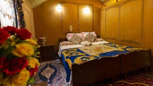 A traditional room with a wooden bed, a nightstand, a wall-mounted lamp, and a floral arrangement. - N Mumbai Group Of House Boat (Srinagar)
