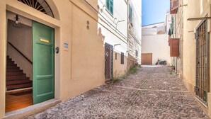 Una estrecha calle adoquinada flanqueada por edificios, uno de ellos con una puerta verde y una escalera que sube a un nivel superior.