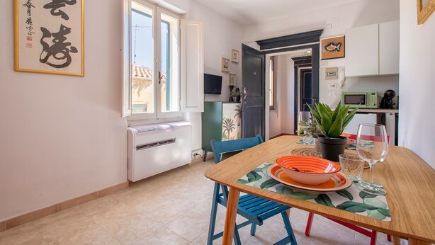 Un comedor con una mesa preparada para dos, una planta en maceta y un televisor al fondo.
