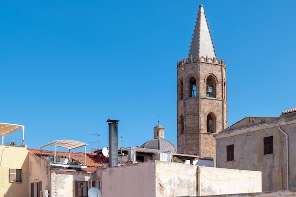 A historic tower with a bell, a dome, and a cross on top, surrounded by buildings with a clear blue sky.