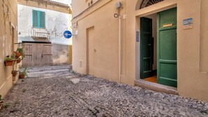 Una estrecha calle adoquinada con un edificio que tiene una puerta verde y un letrero azul que indica un giro a la izquierda.