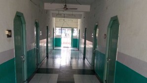 A long, narrow hallway with green and white walls, tiled floors, and doors on both sides leading to rooms. - Raj Kamal Lodge (Chirala)