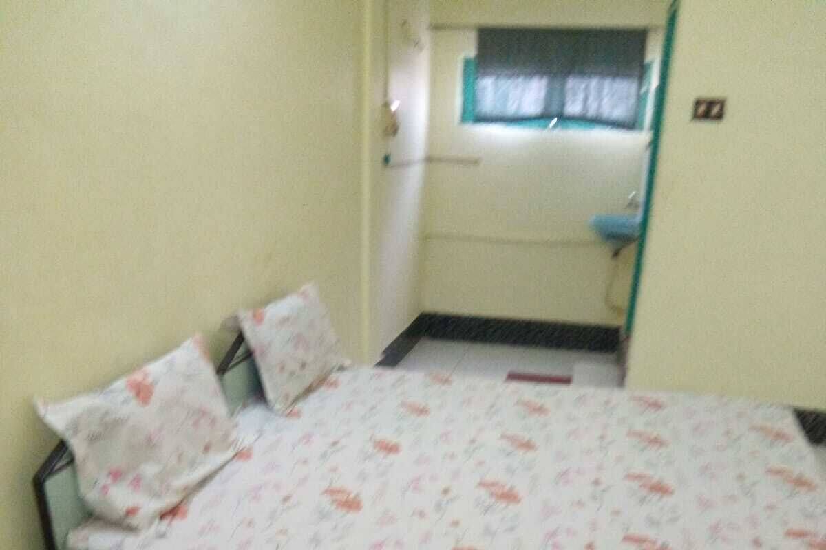 Una camera piccola con un letto singolo, una coperta a fiori, una sedia di legno e una finestra con tenda.