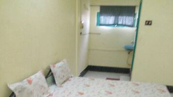 A small, single-bed room with a floral bedspread, a wooden chair, and a window with a curtain.