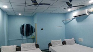 A room with two beds, ceiling fans, and an air conditioning unit. - Raj Kamal Lodge (Chirala)
