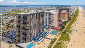 A high-rise hotel with multiple floors, a swimming pool, and a beach area with umbrellas.