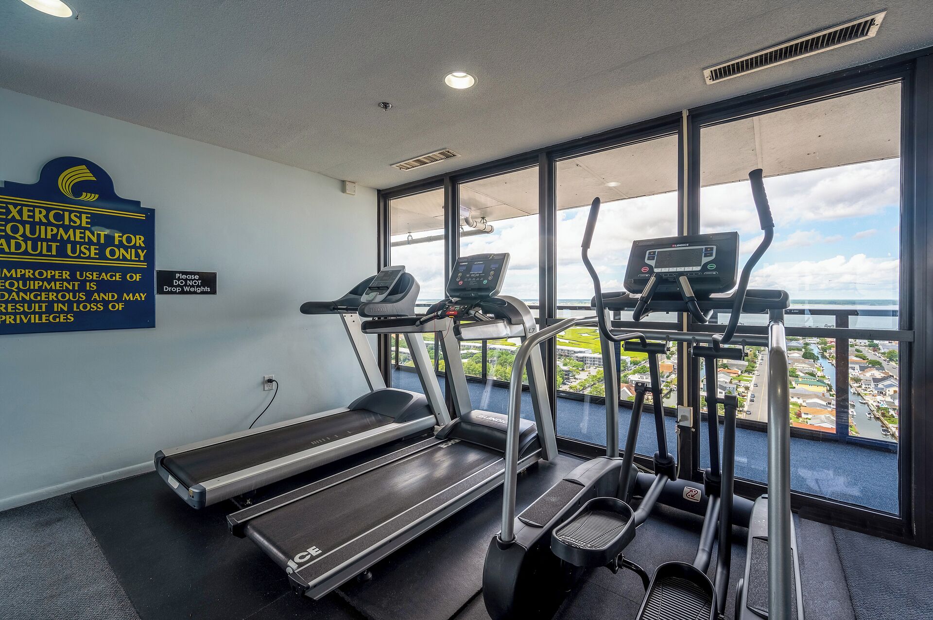 Un gimnasio con cintas de correr, máquinas elípticas y una banca. Hay un cartel en la pared advirtiendo sobre el uso incorrecto de los equipos.
