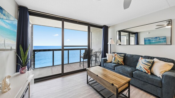 A modern living room with a large sliding glass door leading to a balcony with a view of the ocean.
