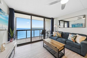 A modern living room with a large sliding glass door leading to a balcony with a view of the ocean.