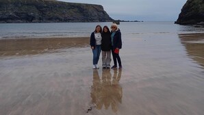 Un gruppo di persone in piedi su una spiaggia sabbiosa, con scogliere rocciose sullo sfondo.