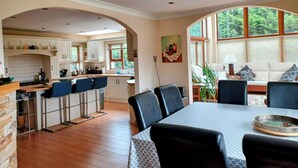 Un'ampia cucina con zona pranzo, caratterizzata da un tavolo grande e sedie, un divano e vista sul verde attraverso ampie finestre.