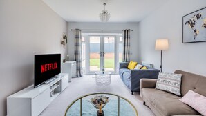 Una sala de estar moderna con un televisor de pantalla plana, un sofá, una mesa de centro y vistas al exterior a través de una puerta de cristal.