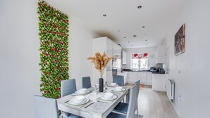 Un comedor moderno con una mesa larga dispuesta para seis personas, rodeada de sillas azul claro. A la izquierda, una pared decorativa verde con flores rojas.