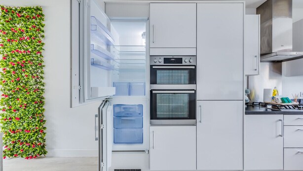Una cocina moderna con armarios blancos, horno empotrado y refrigerador.