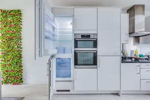 Una cocina moderna con armarios blancos, horno empotrado y refrigerador.