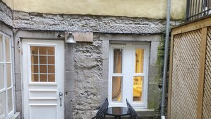 Un patio con un muro de piedra, una puerta blanca, una ventana con cortinas y una mesa con sillas.