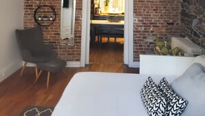 Un dormitorio con cama, candelabro, pared de ladrillo y vista a la cocina.