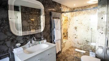 A bathroom with a marble sink, a large mirror, a glass shower enclosure, and a white toilet.