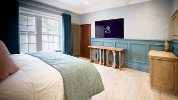 Une chambre d’hôtel avec un grand lit, un téléviseur fixé au mur, un banc en bois et une fenêtre avec des rideaux.