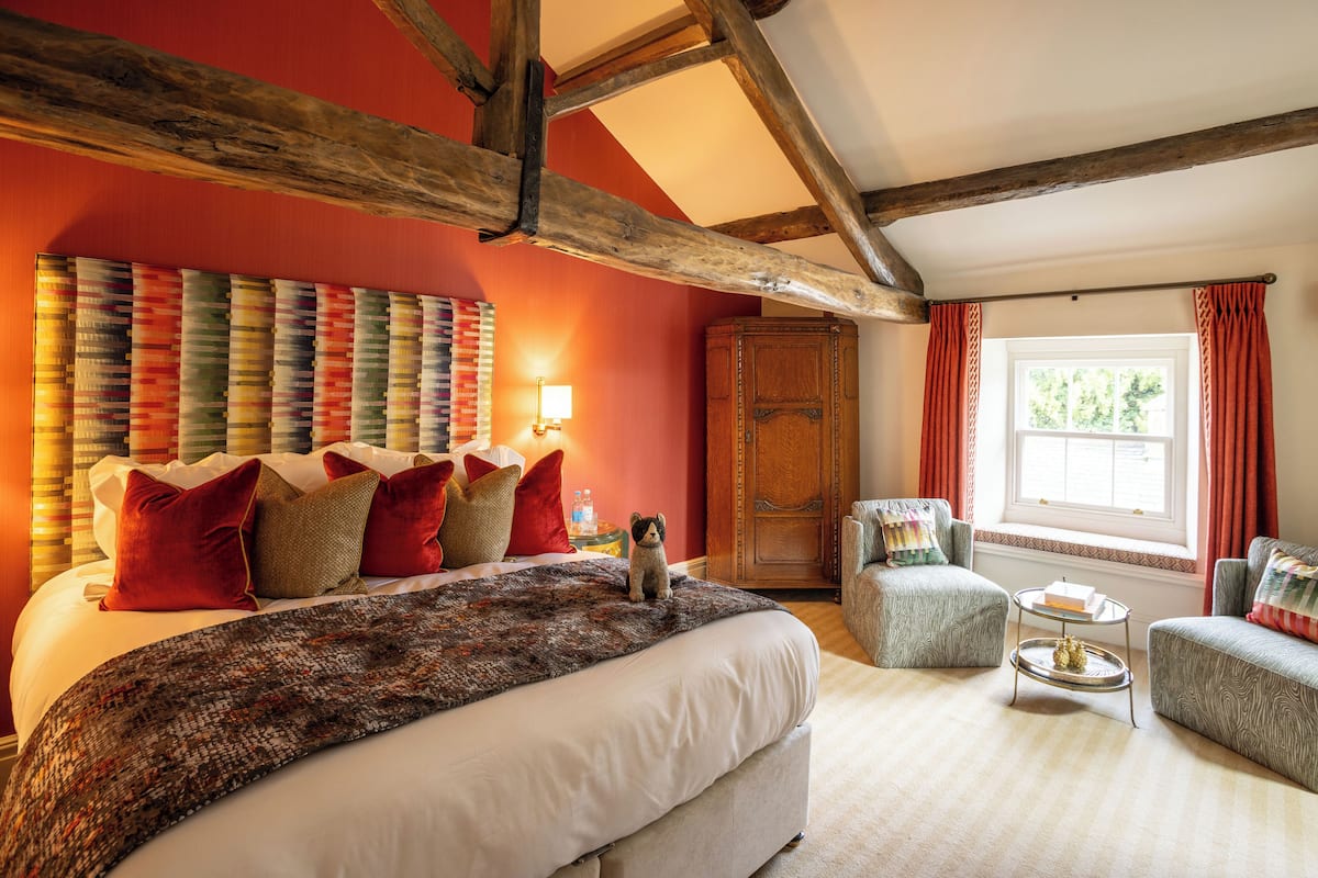 Ein Schlafzimmer mit einem großen Bett, Holzboden, einem Fenster mit Vorhängen und einem kleinen Tisch mit einem Buch und einer Flasche.