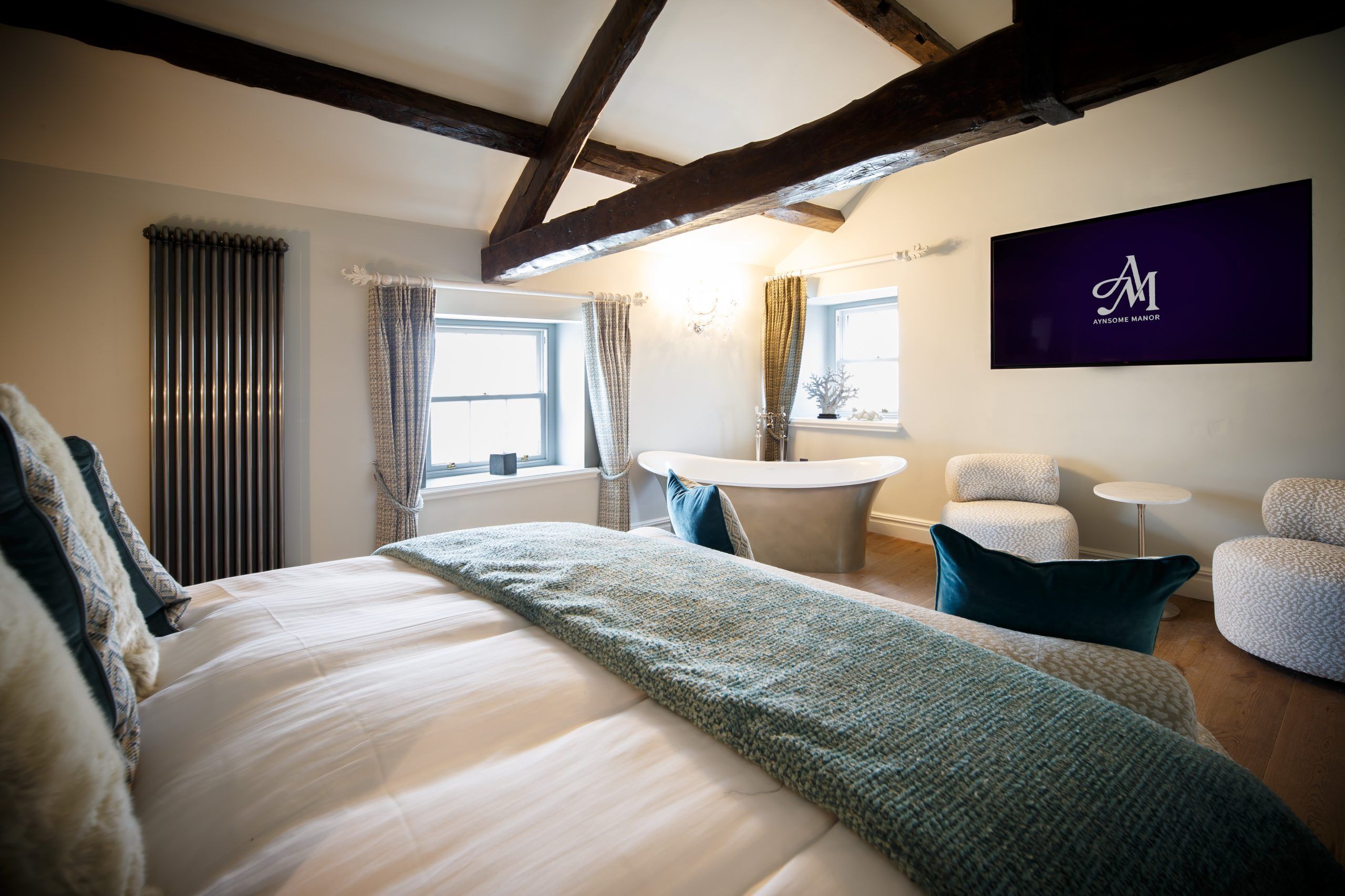 A bedroom with a large bed, a round table, two chairs, and a wall-mounted TV.