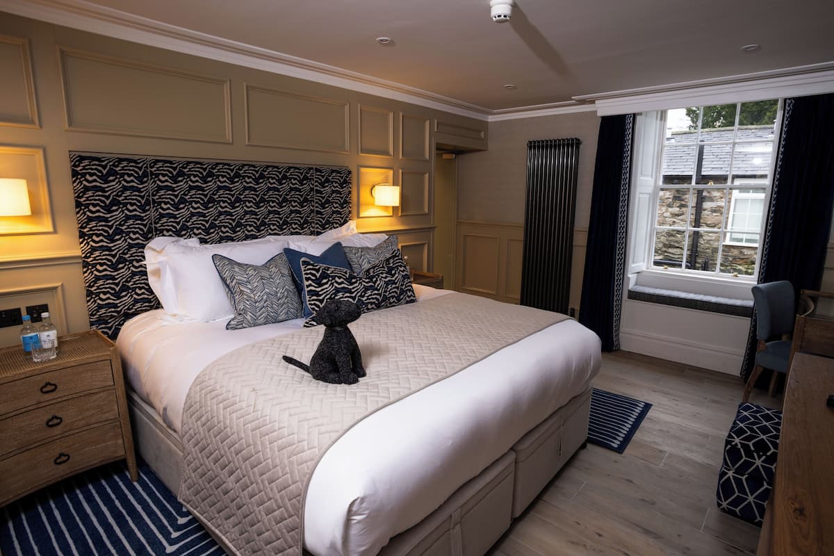 Ein Schlafzimmer mit einem großen Bett, einem Zebra-Muster am Kopfteil, zwei Nachttischlampen, einem Nachttisch, einem Fenster mit Vorhängen und einem kleinen Schreibtisch mit Stuhl.