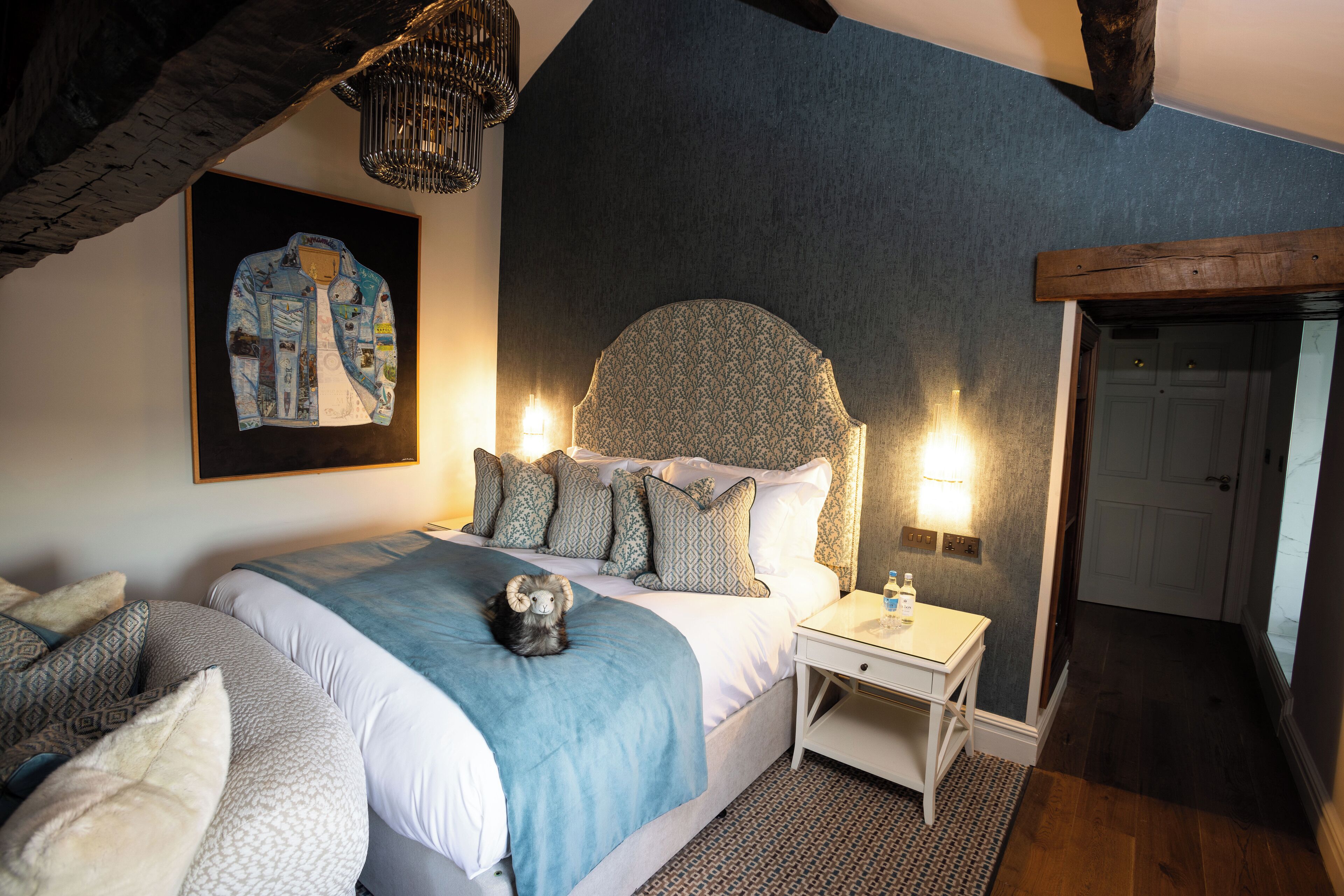 A bedroom with a large bed, a nightstand, a teddy bear, a wall-mounted painting, and a door.