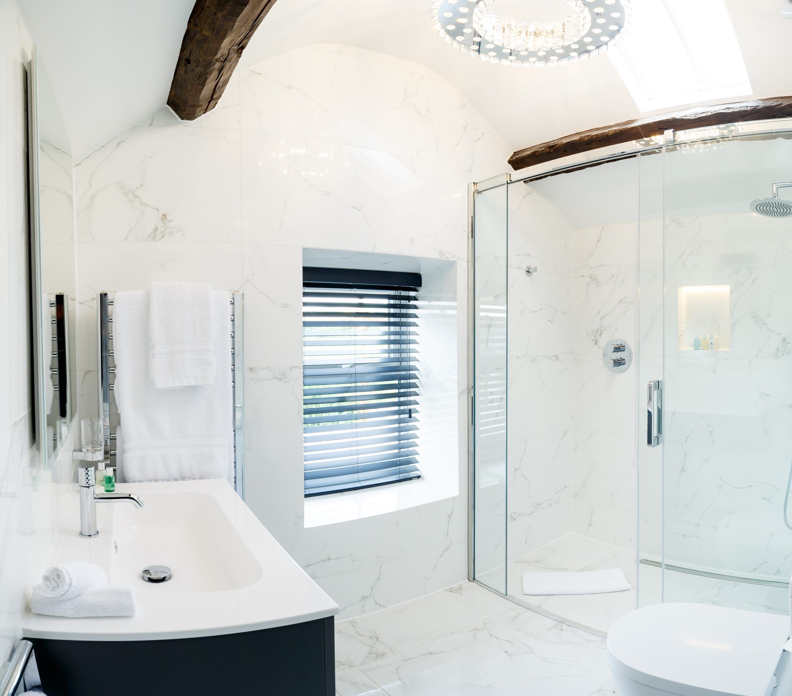 Une salle de bain moderne avec une douche en verre, un grand lavabo et une fenêtre avec des stores.