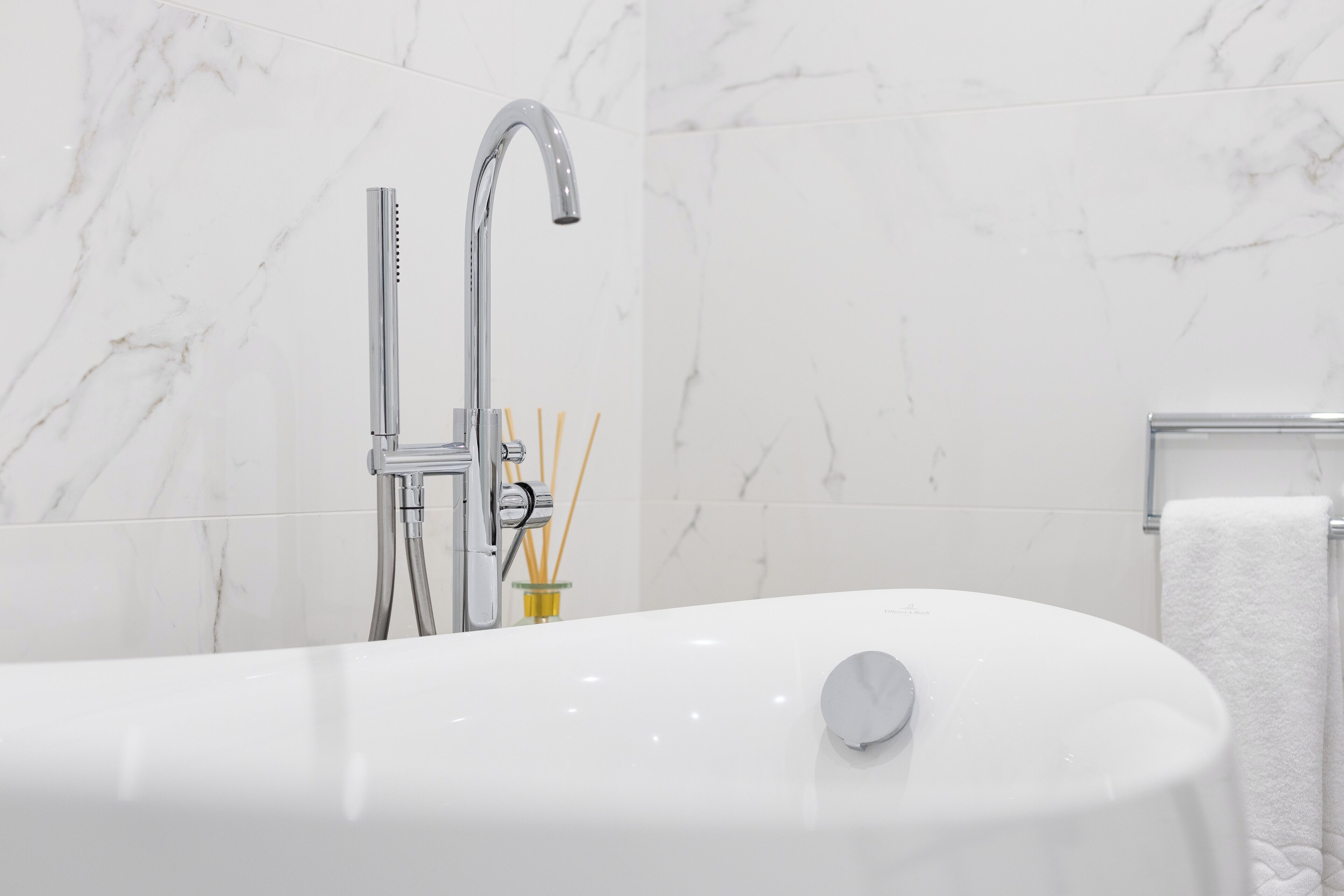 Un baño moderno con una bañera independiente, un grifo cromado y un recipiente de vidrio con difusores de caña.