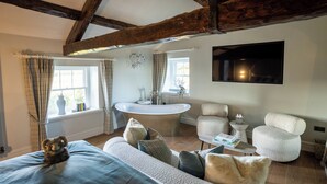 Ein Schlafzimmer mit einem großen Bett, einer Sitzecke mit Stühlen, einem runden Tisch und einem an der Wand befestigten Fernseher.