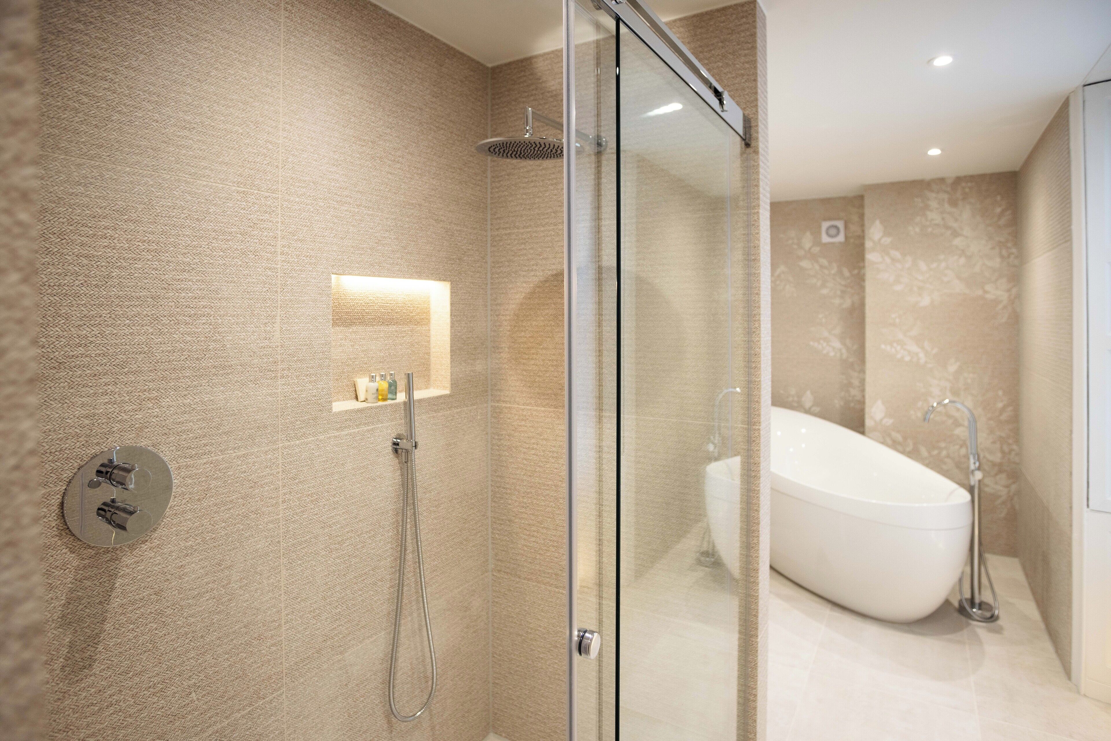Une salle de bain moderne dotée d’une douche à parois de verre, d’une baignoire sur pieds et d’une étagère murale pour les articles de toilette.