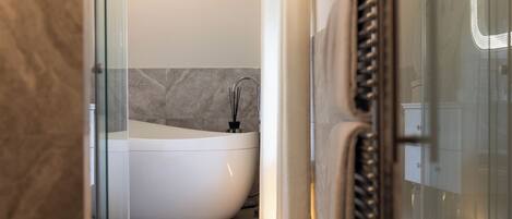 Un baño moderno con una bañera independiente, revestimiento de mármol y cabina de ducha de vidrio.