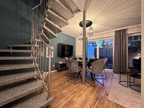 A modern interior with a stone staircase, a dining area with chairs and a table, and a large window. - Luxx Downtown - Design apartment right in the city (Bad Zwischenahn)