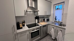 Moderni keittiö, jossa on ruostumattomasta teräksestä valmistetut kodinkoneet, valkoiset kaapit ja ikkuna, josta tulee luonnonvaloa.