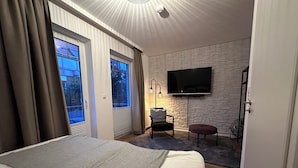 Hotellihuone, jossa on sänky, tuoli, seinälle asennettu televisio ja ikkuna, jossa on verhot.